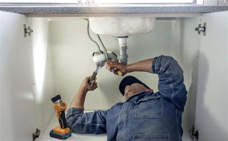 Plumber repairing pipes beneath a bathroom sink in Pembroke Pines