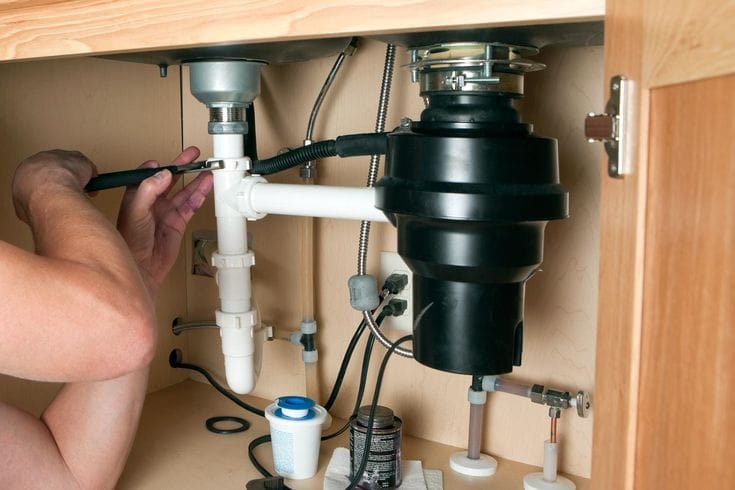 Plumber installing a garbage disposal beneath a kitchen sink in Pembroke Pines