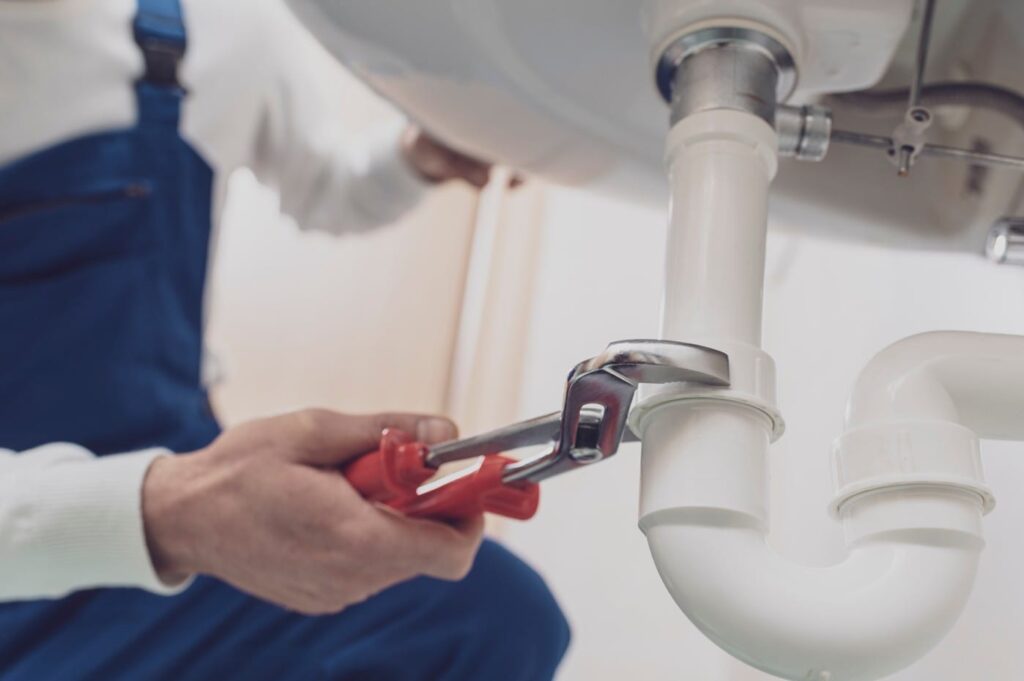 Plumber repairing a white drain pipe beneath a sink in Pembroke Pines