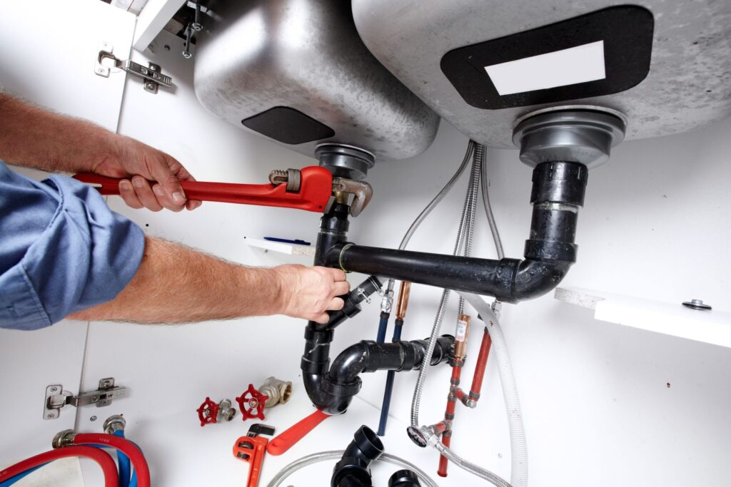 Plumber repairing drain pipes beneath a kitchen sink in Pembroke Pines